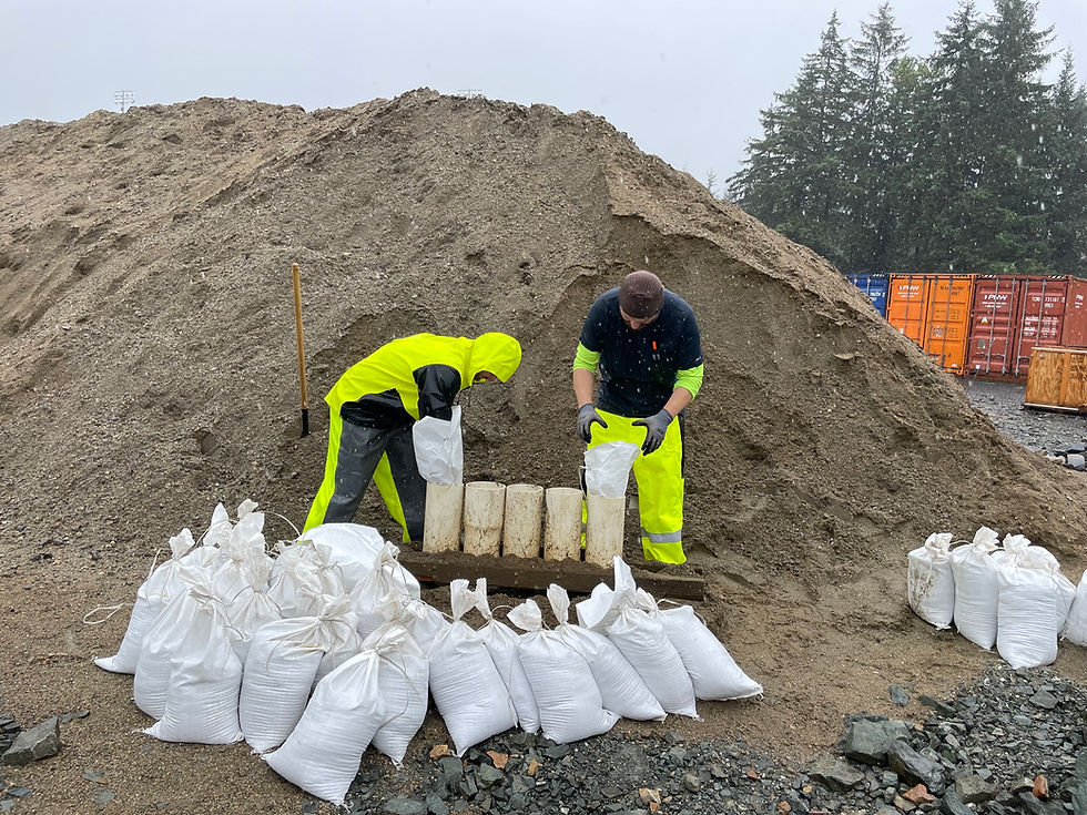 John Somerlot, left, an equipment operator for the city’s streets department, and Jeffrey Thole, a city engineering department project manager, fill sandbags to anchor black plastic sheeting wrapped around super sacks staged along the river to close a gap in HESCO barriers. The gap was kept open to allow hikers to cross on the pedestrian bridge connecting Kaxdigoowoo Heen Dei (Brotherhood Bridge Trail) and Dimond Park trails. The bridge has been closed for safety as the river rises. (Laurie Craig / Juneau Independent)
