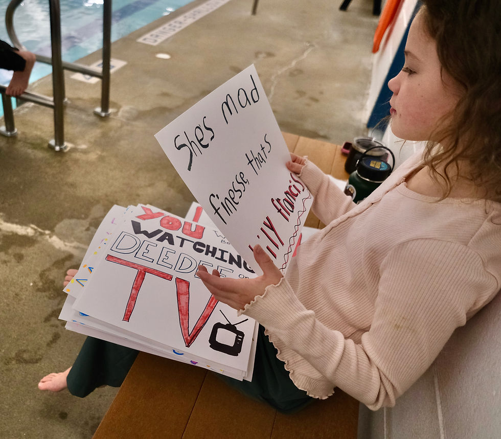 Assistant swim coach Amber Kelly's daughter, Lucy Dyer, 8, looks at posters during Juneau-Douglas High School: Yadaa.at Kalé swim practice Wednesday, Nov. 5, 2025, at Augustus Brown Pool. The Crimson Bears made the posters for each other. The JDHS swim and dive teams will compete at the state championships Nov. 7-8 at Anchorage's Bartlett High School pool. (Klas Stolpe / Juneau Independent)