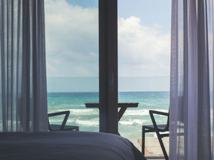 2 chairs at window in hotel bedroom facing a beach scene