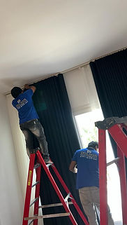 Two men focused on the installation of a window curtains, demonstrating teamwork in a bright indoor setting