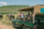 Travellers in an open safari vehicle watching elephants during a drive-in safari en route to their lodge
