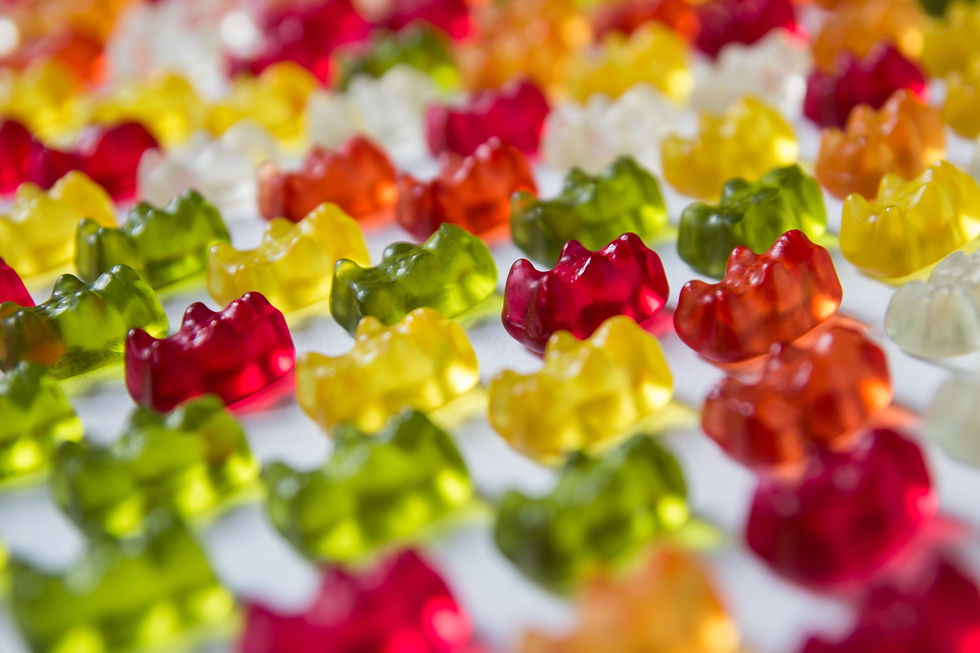 Colorful cannabis gummy bears in red, green, yellow, and orange are scattered in rows on a white background, creating a playful and vibrant scene.