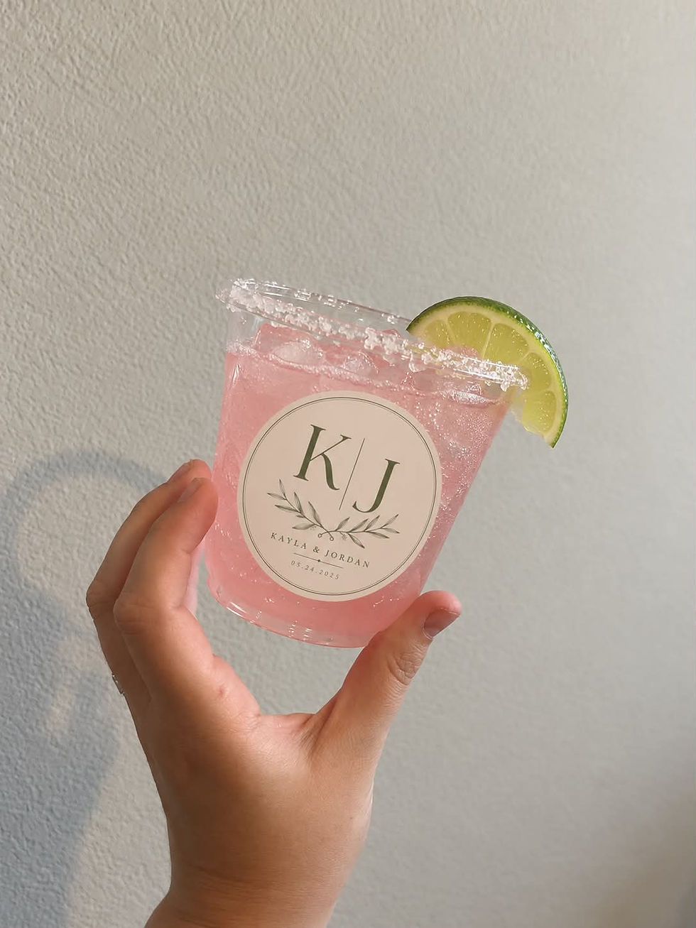 Photo of a hand holding a pink cocktail in a custom branded cup with initials KJ