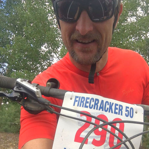 Cyclist riding a mountain bike through an open Colorado trail on a sunny day, wearing a race bib — a snapshot of energy, endurance, and connection to the Rocky Mountain landscape.