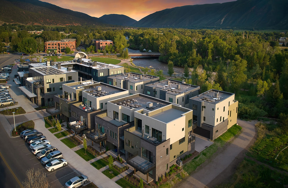 Aerial view of the Gallery Building in Basalt, Colorado at sunset, showing modern mixed-use architecture with River Lofts residences, CMC Morgridge Commons, and Design Workshop offices, framed by the Roaring Fork River and surrounding mountains.