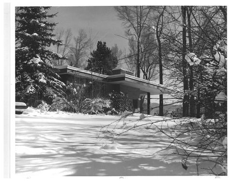 Winter view of the William Field Residence from the snowy yard, with trees surrounding the home and mid-century rooflines peeking through the landscape.