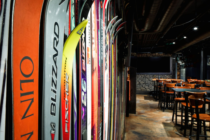 Close-up of ski wall installation featuring vintage skis at Buck Bar & Kitchen in Aspen, with warm lighting and gabion stone wall detail in the background.