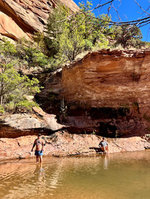 Two people enjoy a peaceful moment at a natural pool surrounded by red rock cliffs