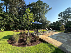 Natural stone backyard patio with lounge chairs, umbrella, and mulched planting beds; residential installation in Augusta, GA