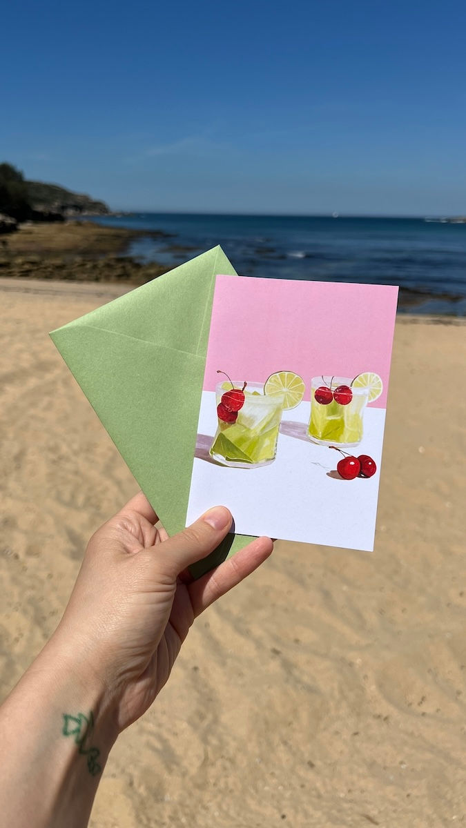 Green Melon Cooler cocktail with cherries, greeting card on pink and white background with green envelope