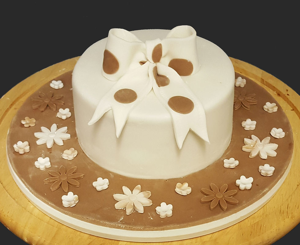 Small, white sugar paste cake with brown board and poorly made spotty sugar paste bow
