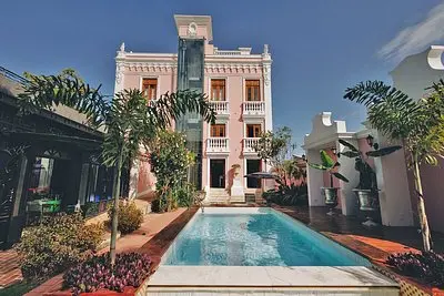 uma casa rosa com jardins floridos na entrada, piscina com agua cristalina