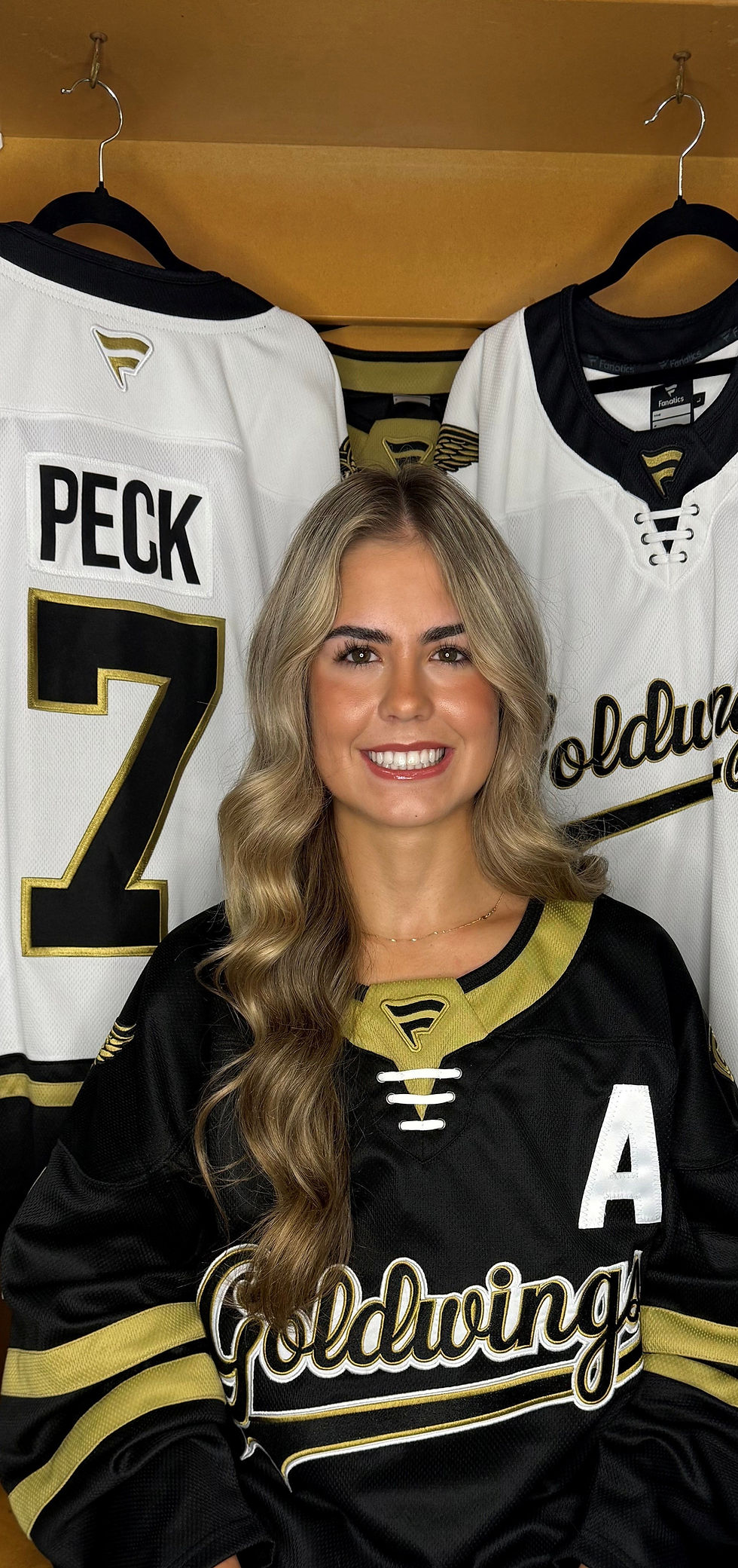 Portrait of Liv sitting in a hockey locker room wearing a black Goldwings jersey, smiling