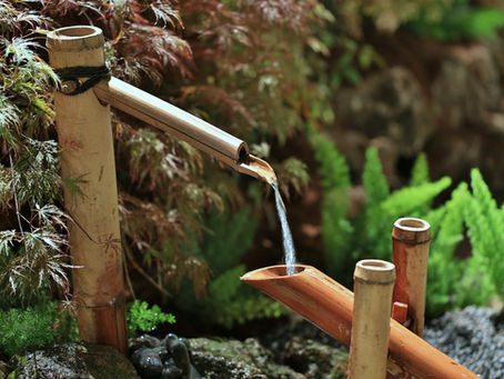 A small bamboo fountain trickling water into a stone basin, illustrating a compact, tranquil water feature.