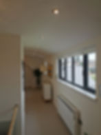 A long landing with downlights installed perfectly straight all the way down the centre of the corridor. There is an electric radiator installed under a window with the power supply next to it.