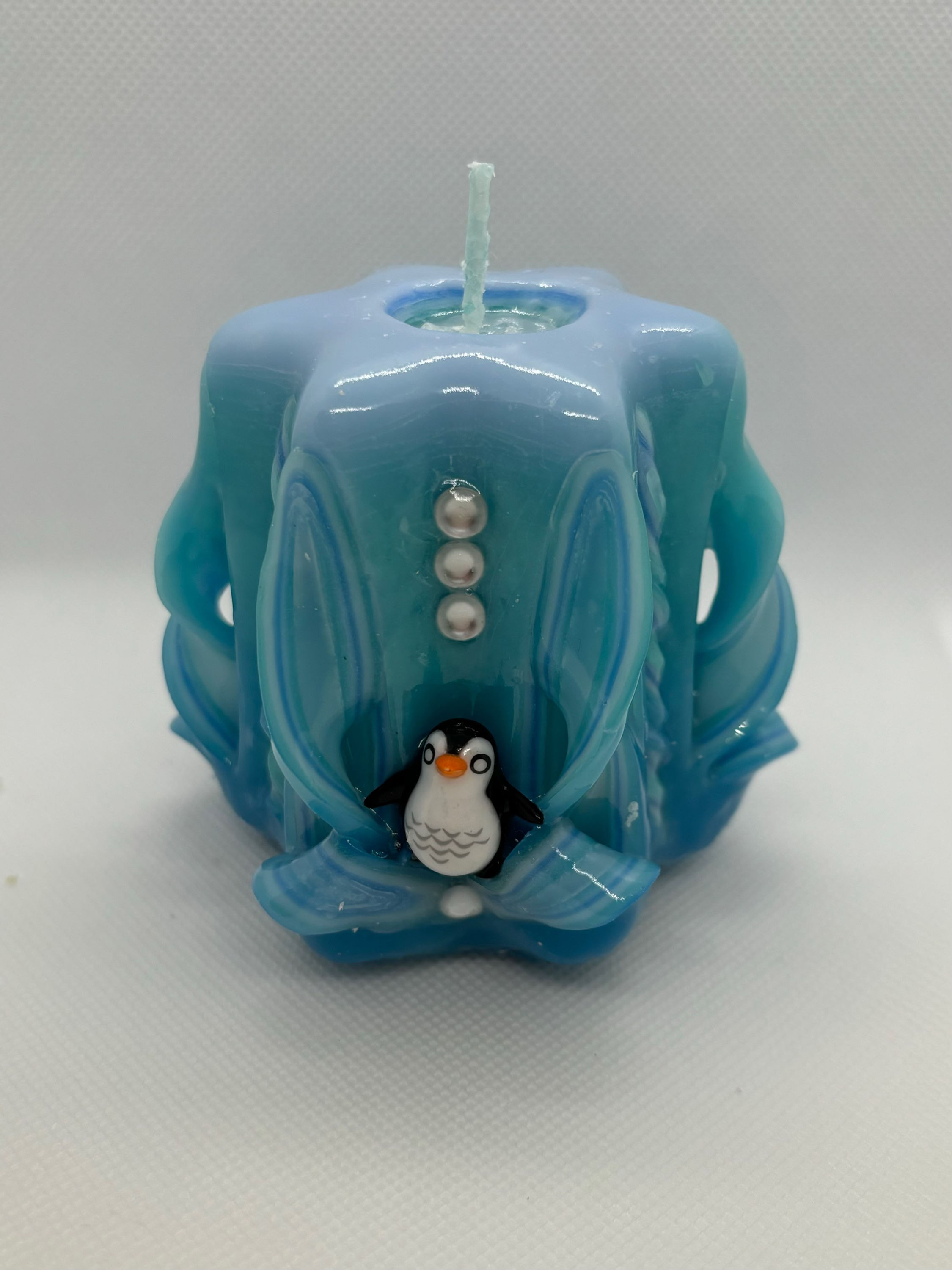 A hand carved blue candle with a penguin sitting on the front