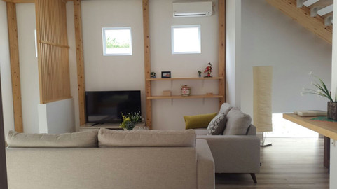 Japandi-style living area in a home in Delta Mas, Cikarang. Neutral-tone furnishing with cozy ambience, showing sofa, shelving, television and lights.