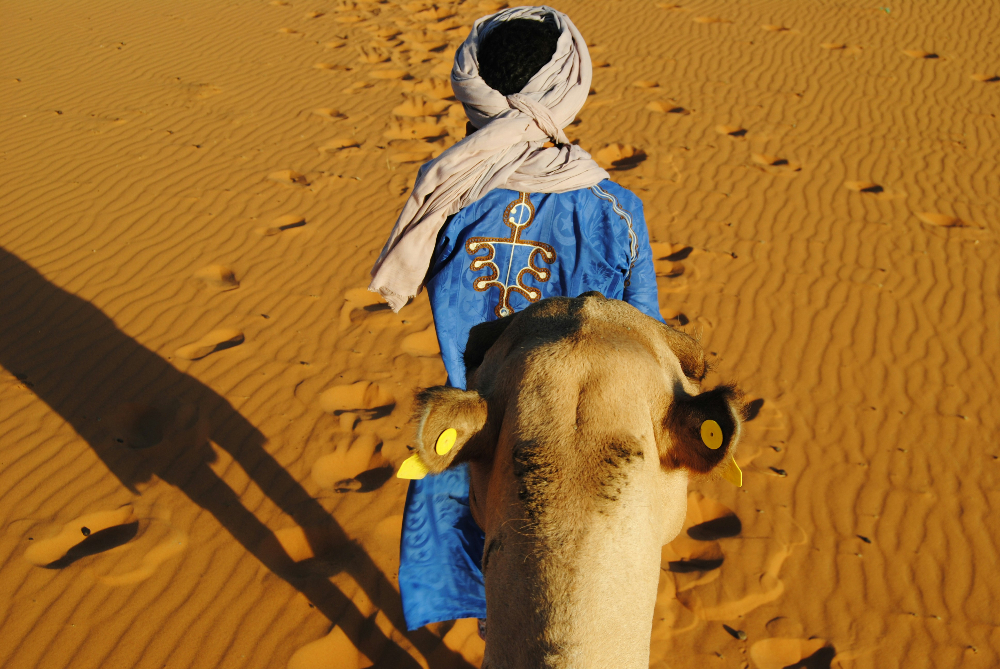 A local man wearing traditional clothes with his camel in the sahara in Morocco