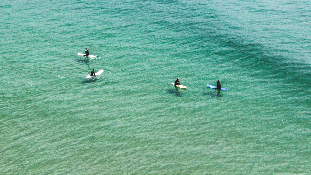 Four surfers in wetsuits in Imsouane morocco, sit on colorful boards in calm, clear turquoise ocean water, creating a peaceful and serene mood.