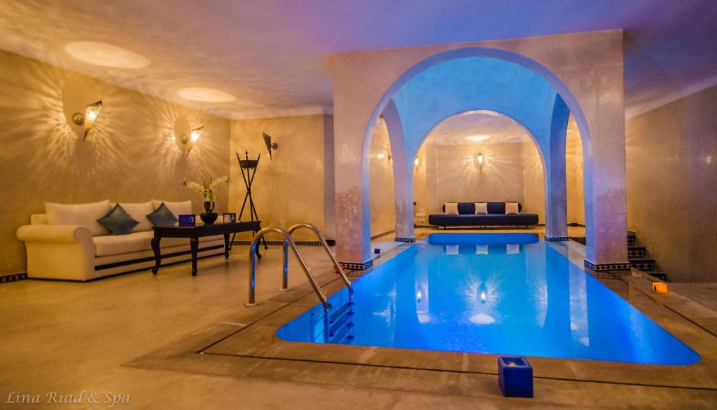 Elegant indoor pool with blue lighting, surrounded by beige walls. A white sofa with blue cushions sits nearby, creating a serene atmosphere.