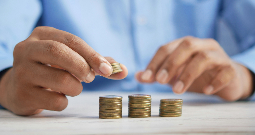 Hands stacking coins on a table, with three neat piles. Person wears a blue shirt. Scene suggests focus and precision.