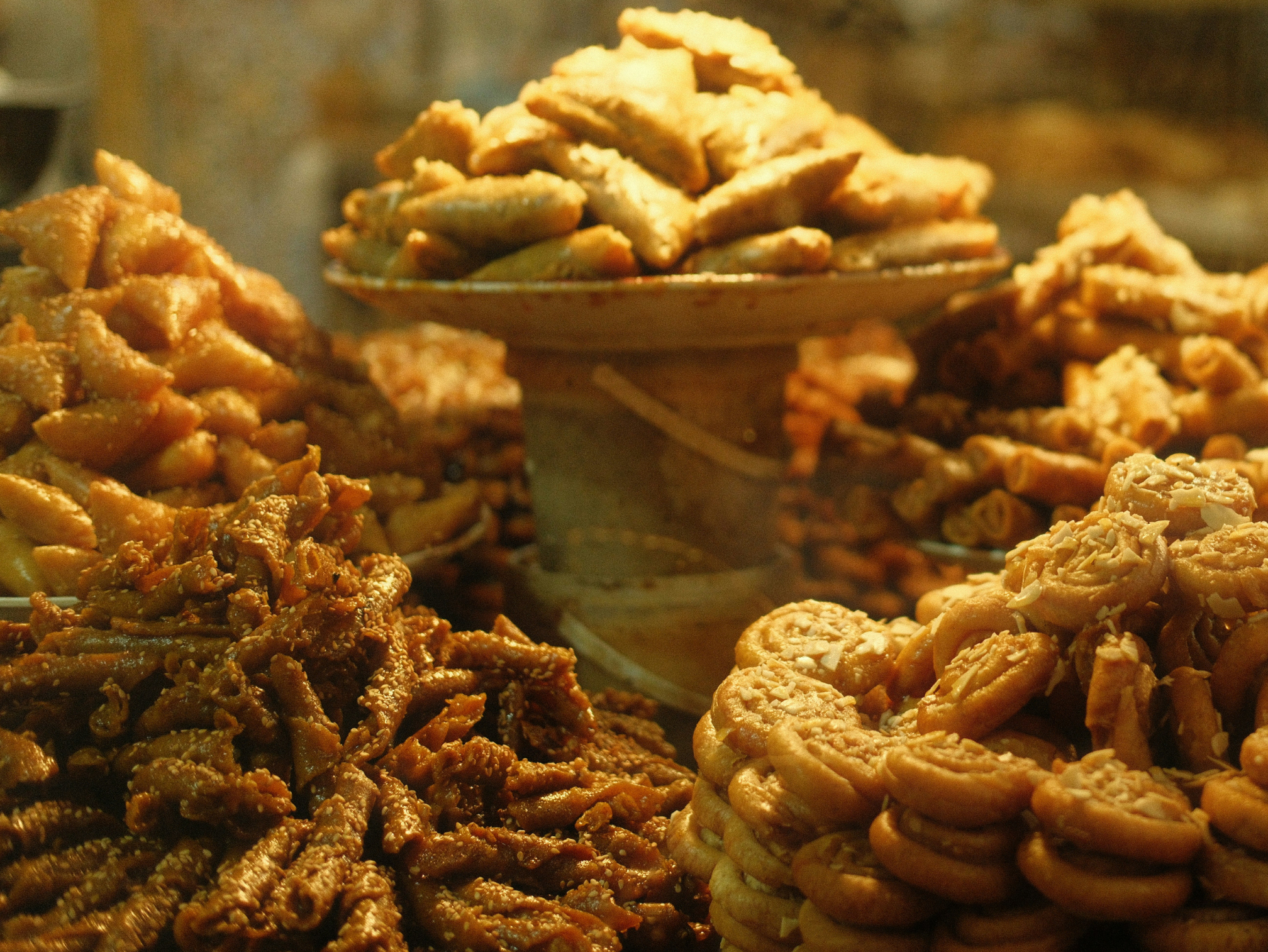 Assorted golden chebakia and other Moroccan pastries and sweets piled on a display stand, creating a warm and inviting atmosphere with rich textures and details.