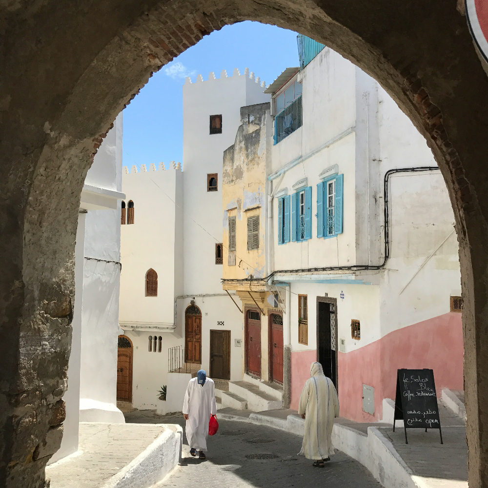 Men wearing traditional white jellabas, walking in tangier alleys