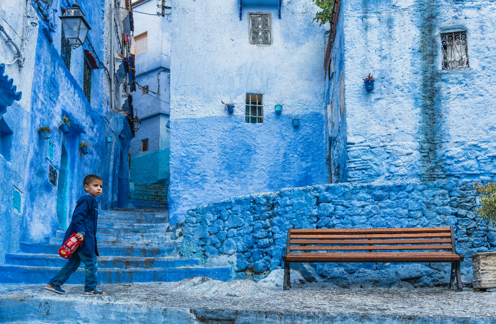 a blue alley in the city of chefchaouen. There's a child walking between the blue houses.