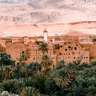 A landcape of a desert village in Morocco next to a valley full of palm trees