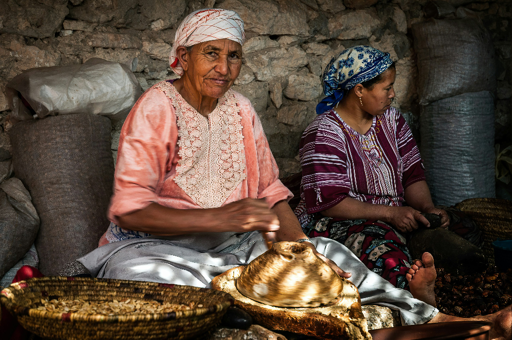 two women we<aring traditional clothes in essaouira grinding argan seeds to make argan oil