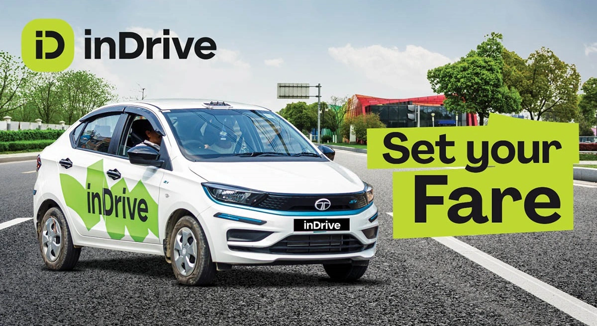White car with ‘inDrive’ logo driving on road, green trees in background. Text: ‘Set your Fare.’ Bright, sunny setting.