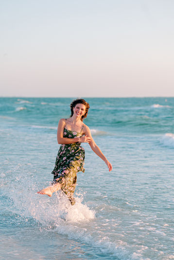Senior portrait of girl with long hair wearing a green dress twirling in the sand at Fort De Soto beach by Tampa senior portrait photographer Nina Bashaw