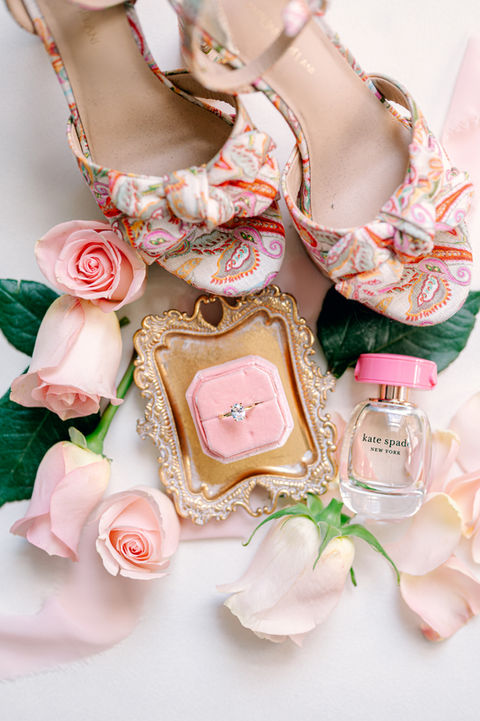 Wedding flatlay with pink shoes, flower petals, pears, and perfume bottle