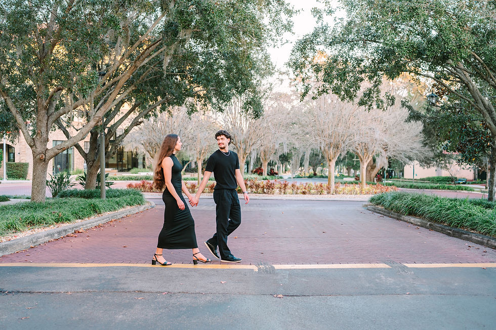 Ellie and Mason walking hand in hand in matching all black outfits at St. Leo University, captured by Tampa engagement photographer Nina Bashaw, with golden hour light highlighting their connection.