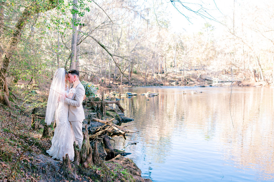 Bride and groom posing together under trees in park