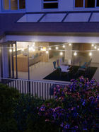 Modern home exterior with lights, patio, and glass doors at dusk.