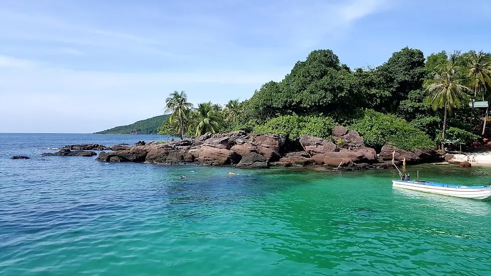 Tropical bay with turquoise water, rocky shore, palm trees, and a small white boat under a clear blue sky.