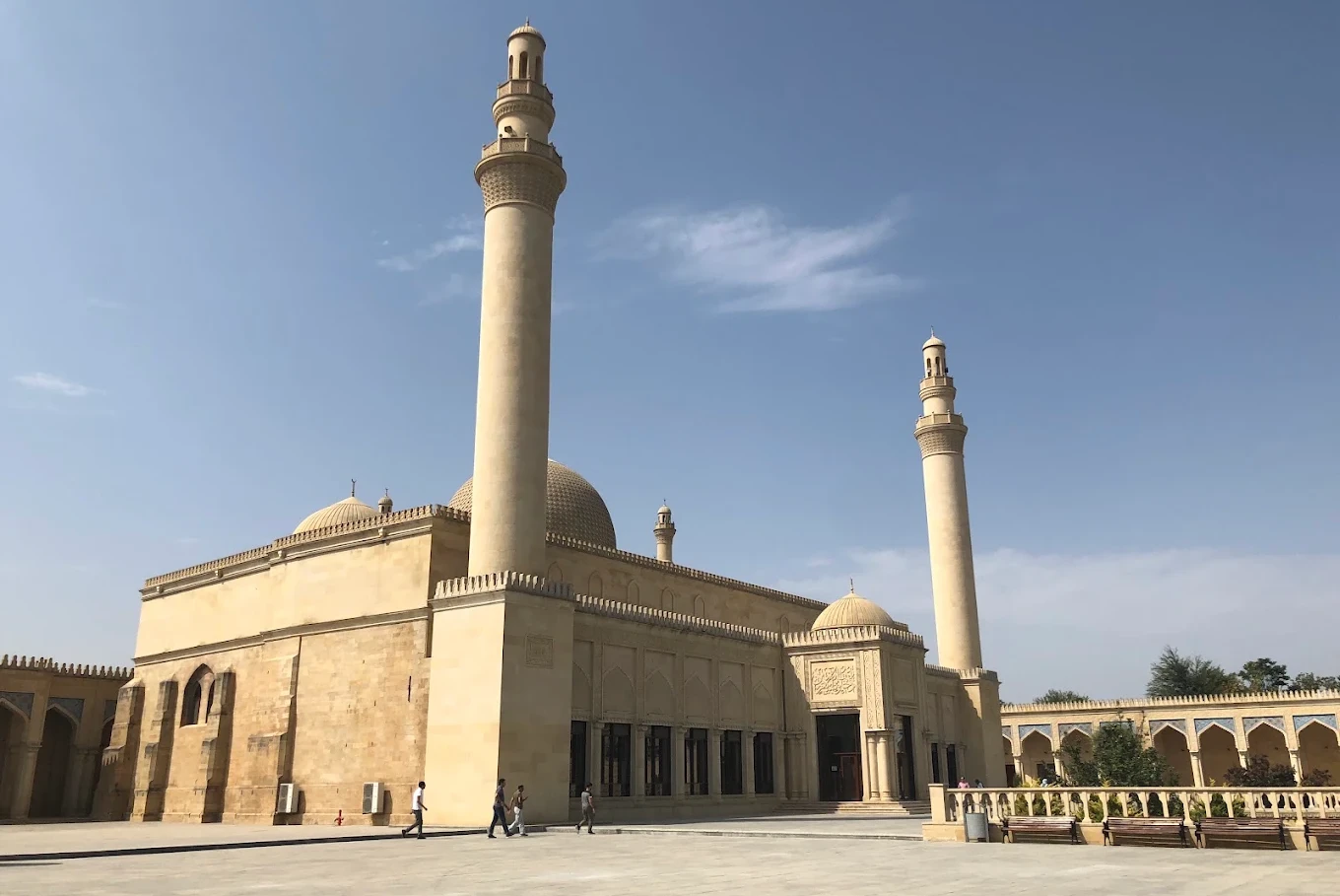 Shamakhi Juma Mosque Historic beige mosque with two tall minarets under a clear blue sky, with a few people walking in the courtyard.