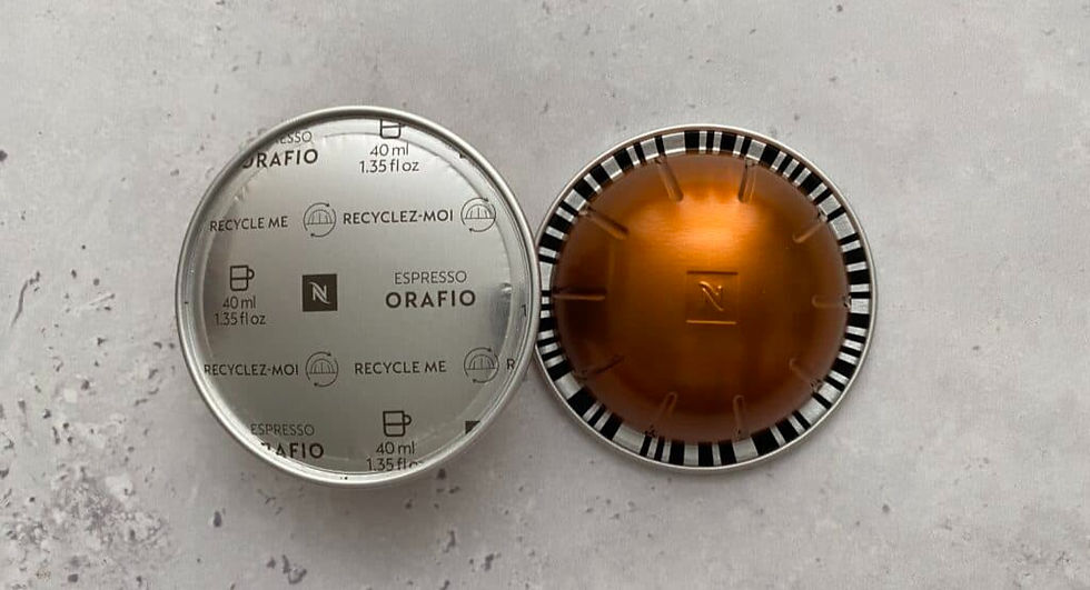 Two Nespresso Orafio pods on a speckled gray surface. One shows a metallic top with text, the other an orange capsule with black stripes.