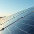 Solar panels reflecting sunlight, angled in a row. Clear blue sky and distant mountains create a serene backdrop.
