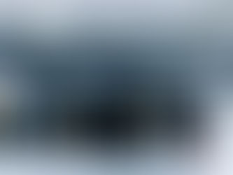 Server room with rows of black and white servers, blue cables overhead. A table and chair are visible nearby, with bright lighting.