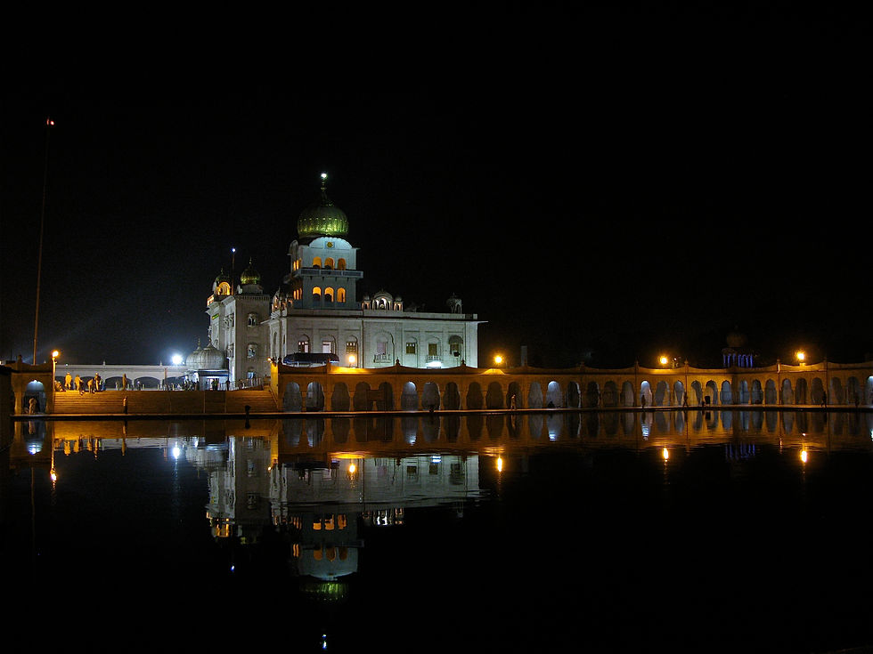Gurudwara Bangla Sahib Illuminated Sikh temple with golden domes at night, reflected in still water, with glowing lamps and a few visitors on the walkway
