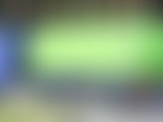 A blue truck with a green hydrogen cylindrical tanker is driving past a forest. The tanker has a ladder, and the truck is on a paved road.