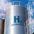 Silver hydrogen storage tanks with "H2 HYDROGEN" text, set against a clear blue sky with clouds. A ladder is attached to the tanks. BLUE HYDROGEN