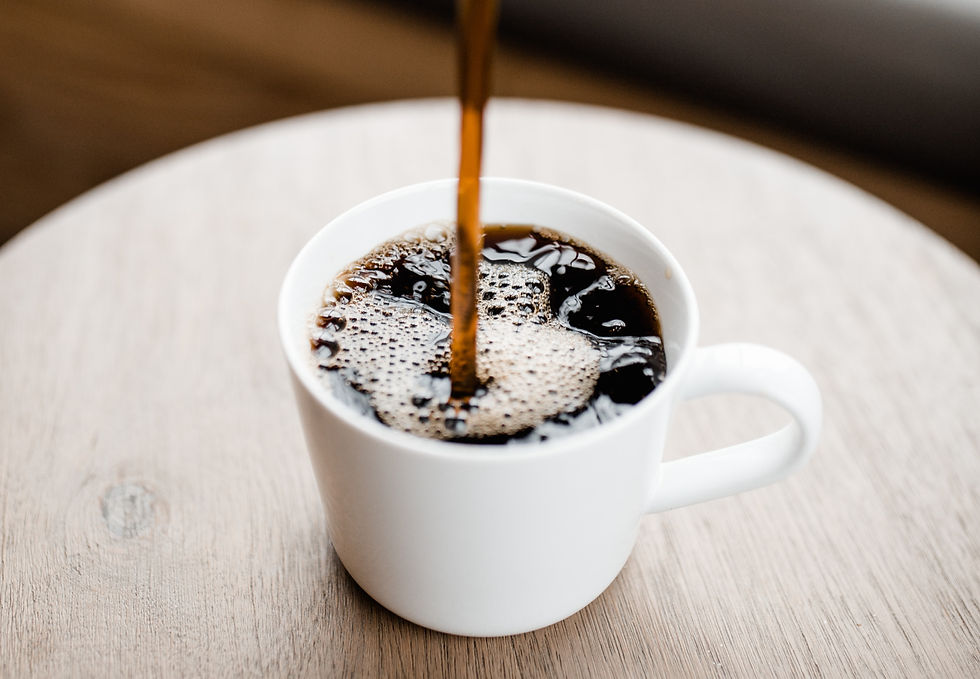 Black Coffee being poured into a white cup on a wooden surface, creating bubbles. The scene is warm and inviting, with a close-up focus.