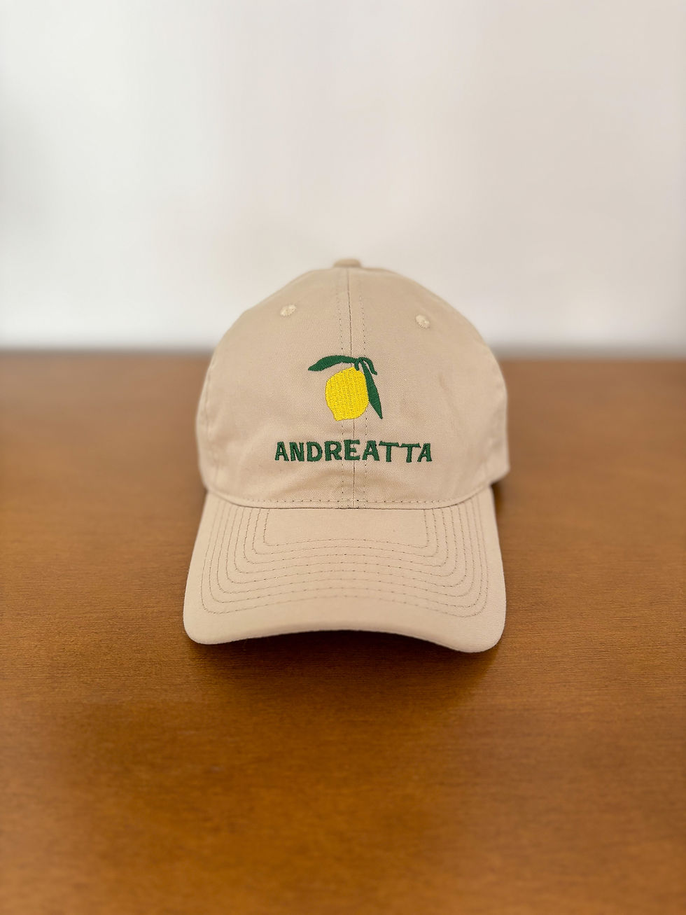 Frente do boné bege modelo dadhat com bordado de um limão verde e amarelo e bordado da Andreatta logo abaixo