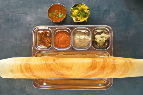 Rolled dosa with sambar and chutneys on a metal tray