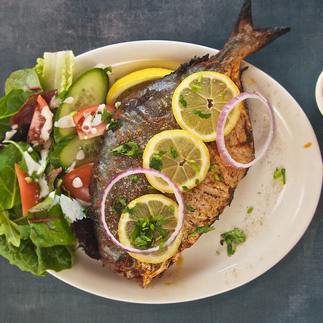 Plated grilled fish with lemon, onion, and green salad