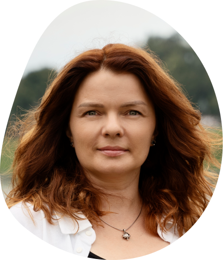 Young woman with blonde hair and a calm expression, against a plain gray background. She wears a black top, and her eyes look forward.