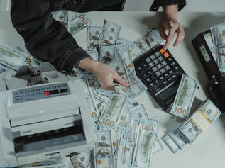 Hands counting cash beside a calculator on a desk